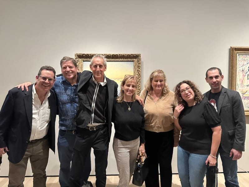 Group of seven people posing together in front of an Impressionist painting in a museum gallery